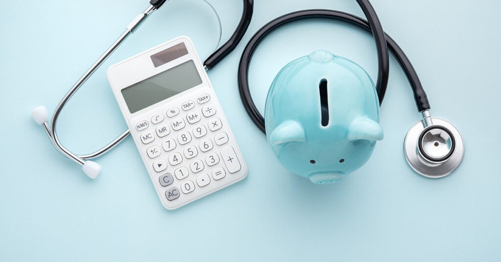 A stethoscope, a white calculator, and a blue piggy bank are displayed against a light blue background.