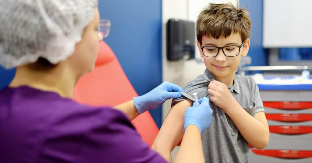 A healthcare worker applies a bandage to a young boy's arm after administering a shot in a medical office.