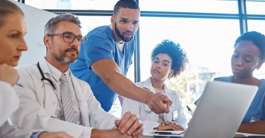 A group of medical professionals in discussion, with one pointing at a laptop screen while others listen attentively.