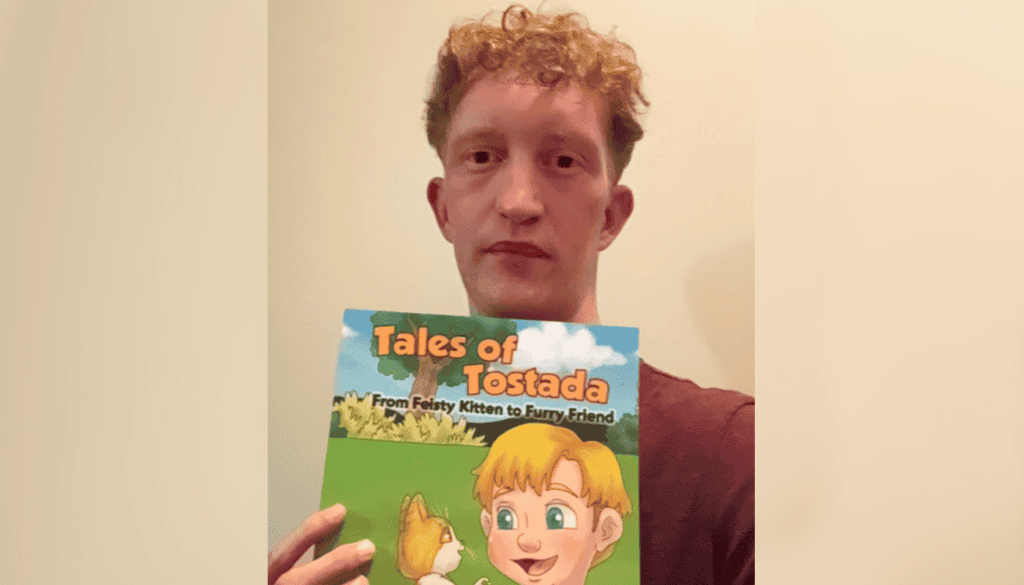 Person holding a children's book titled "Tales of Tostada: From Feisty Kitten to Furry Friend," featuring a cartoon image of a child and a kitten on the cover.