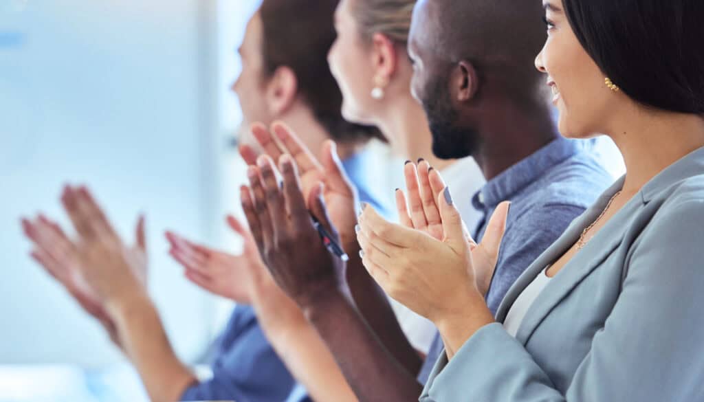 A group of people sitting side by side, attentively clapping and looking in the same direction.