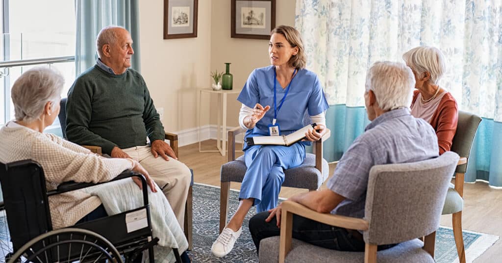 A healthcare professional leads a group therapy session with four elderly individuals seated in a circle.