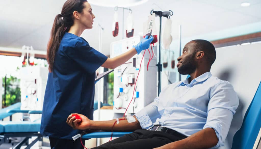 A nurse adjusts an IV for a man donating blood, who is seated and holding a stress ball.