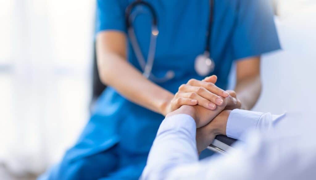 Healthcare worker in blue scrubs holds a patient's hands in a supportive gesture.