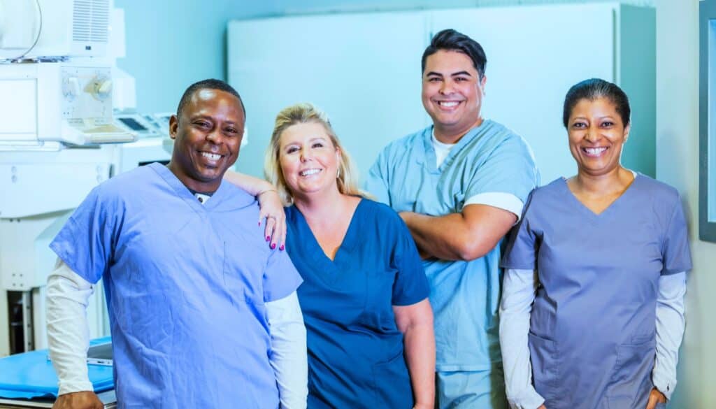 Four healthcare professionals in scrubs stand together in a clinical setting, smiling at the camera.