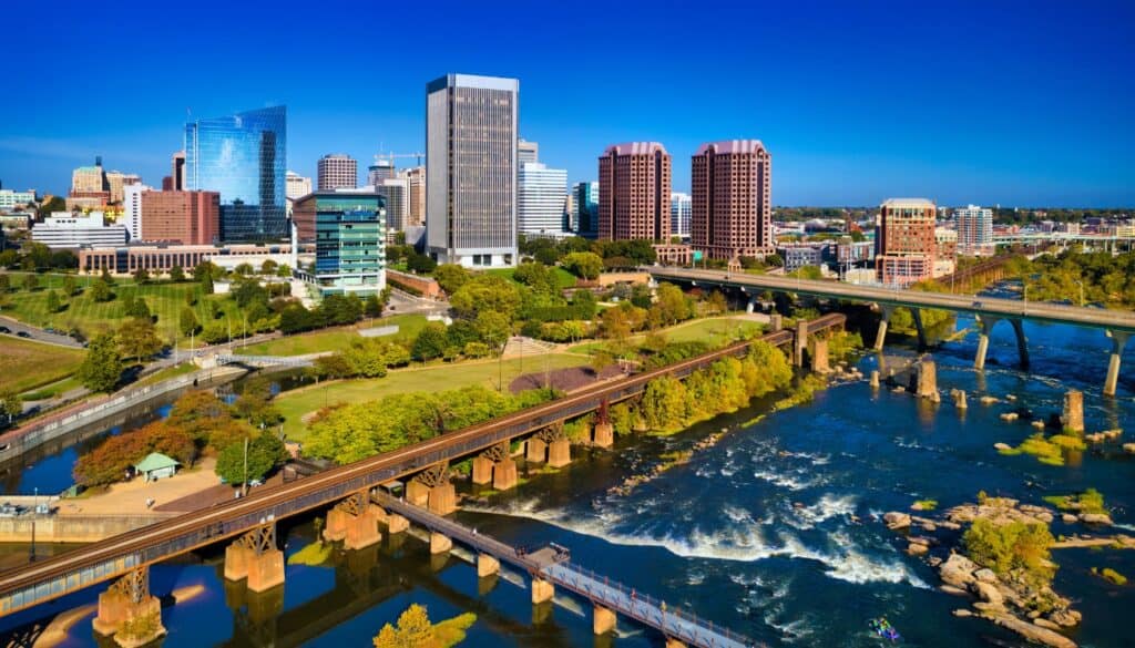 Skyline of a city with modern buildings, bridges over a river with rapids, and green spaces on a clear day.