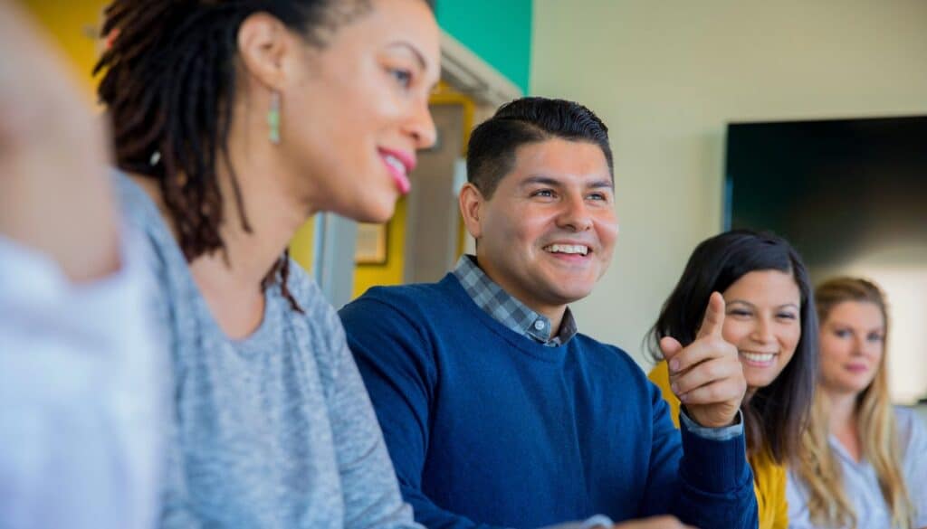 Group of four people sitting indoors, engaged in conversation. One person is smiling and gesturing while others listen and smile.