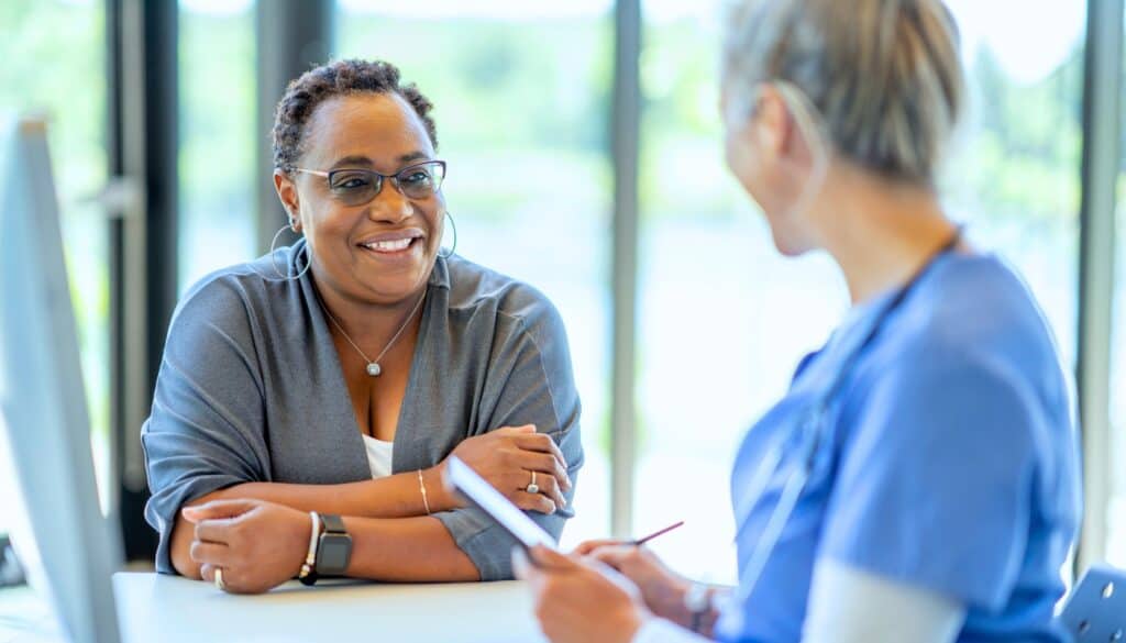 A woman sits across from a healthcare professional in a medical office, engaged in conversation.