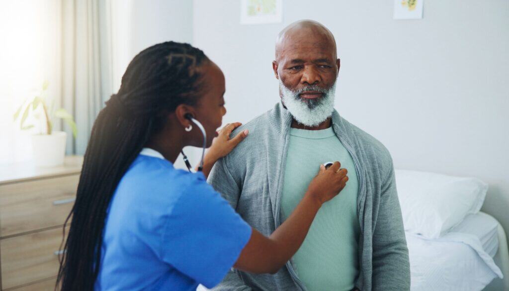 A healthcare worker uses a stethoscope to listen to an older man's chest in a medical setting.