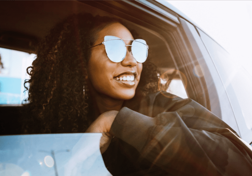 An image of a young woman in a car smiling away from the camera out her window as she travels for her healthcare job